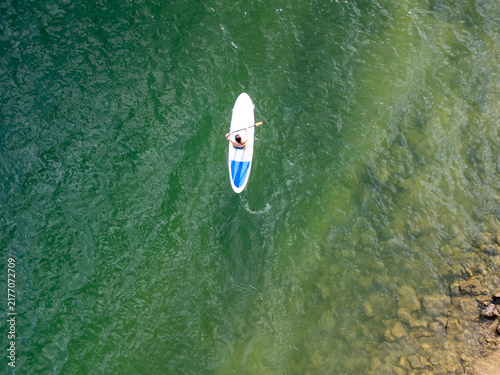 Person paddle surf on green water from aerial view