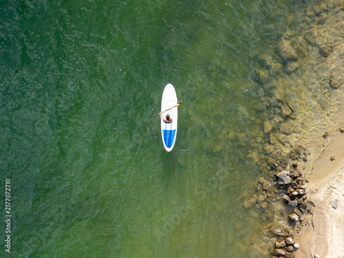 Person paddle surf on calm water near rocky shore