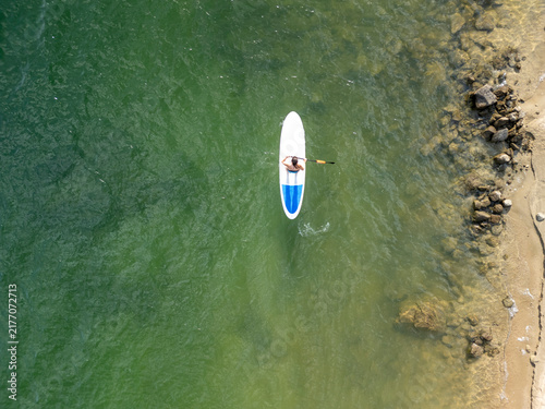 Person paddle surf along rocky coastline on green water