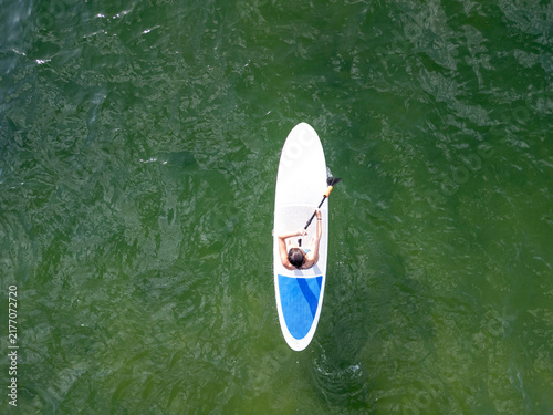 Person paddle surf on green water from aerial view