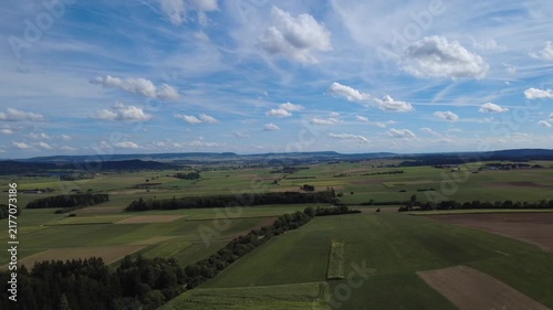 Aerial view of green agricultural fields, open farmland and forest edges under a cloudy sky, showing a peaceful rural landscape with natural patterns and wide countryside scenery.