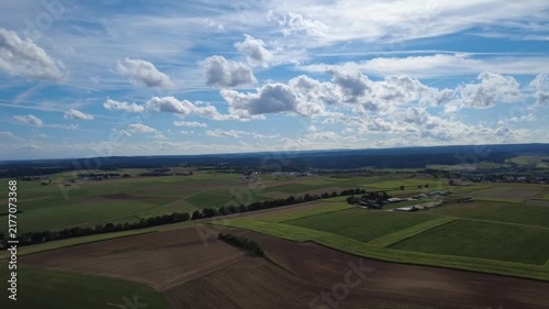 Aerial view of green agricultural fields, open farmland and forest edges under a cloudy sky, showing a peaceful rural landscape with natural patterns and wide countryside scenery.