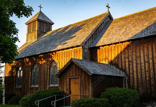 Historic wooden church with cross-topped steeple bathed in warm golden hour sunlight