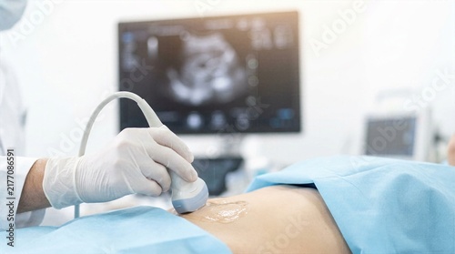 Doctor performing abdominal ultrasound scan on pregnant patient using modern sonography equipment in bright medical clinic room