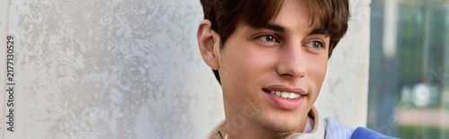 Konstfotografi A young man in a blue shirt smiles while embracing his college experience outsid