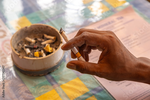 Obraz na plátně a hand holding a cigarette above an ashtray containing cigarette butts and ash