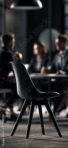 Empty chair in corporate meeting room during discussion. Empty chair at a dark conference table with blurred executives discussing in the background