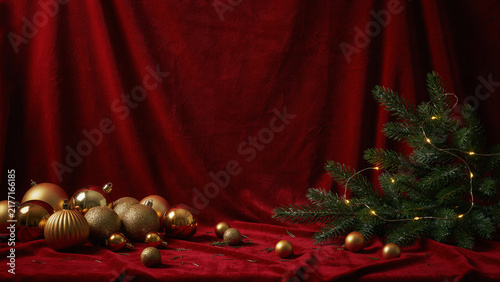 Elegant holiday decor featuring golden baubles and small pine branch with twinkling lights on red velvet cloth