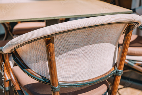 Photography Rattan bistro chair at cafe table, close-up detail of woven backrest and wood frame, outdoor seating
