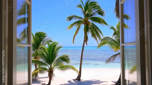Palm trees sway beyond an open window overlooking a tropical beach and turquoise ocean