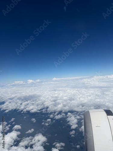 Airplane Window View Above White Clouds and Deep Blue Sky