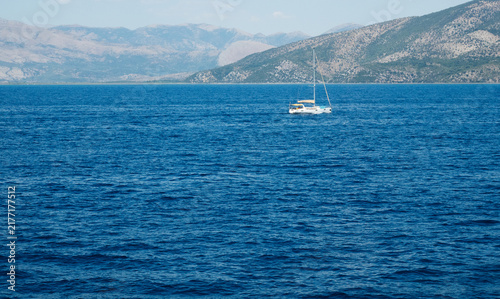 Monohull sailing yacht anchored in clear blue sea near the coast of Corfu island in Greece during a partly cloudy day, summer vacation concept