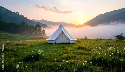 White canvas bell tent on a green mountain meadow with wildflowers at sunrise