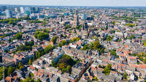 Aerial drone view of Utrecht, Netherlands featuring its historic church tower, red‑roofed buildings, modern skyline, and sunny urban landscape blending old and new architecture.