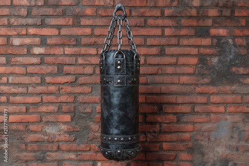 Heavy black leather punching bag hanging in a rustic urban gym with a red brick wall