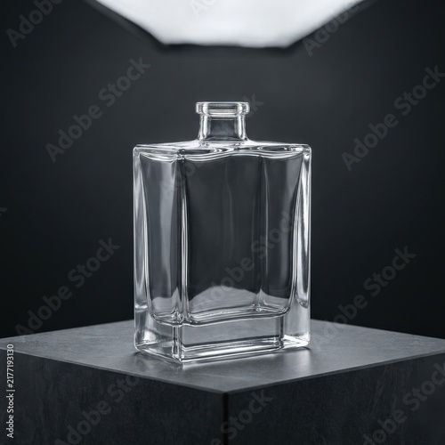 Minimalist glass bottle on a dark stone pedestal for cosmetic product mockup