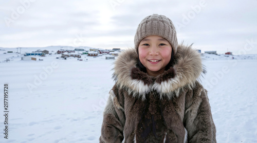 A smiling young indigenous child wearing traditional fur clothing and a knit hat stands in a snowy arctic village landscape, expressing joy and cultural heritage in a cold winter environment.