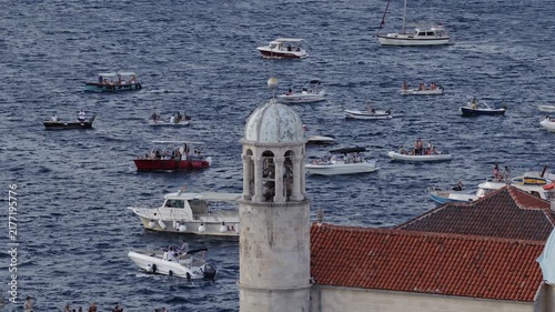aerial telephoto view of the bell tower and red tiled roof of the church on our lady of the rocks island with visitors on the quay and boats on the water behind, bay of kotor, montenegro