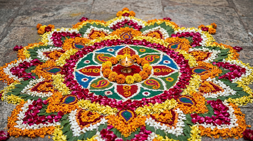 Obraz premium Elaborate floral rangoli floor art with lit diya lamp in the center