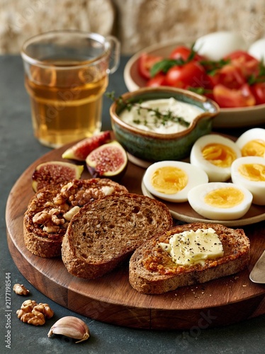 Wooden platter with a variety of food items on it. on the left side of the platter, there is a slice of bread with walnuts and figs on top.