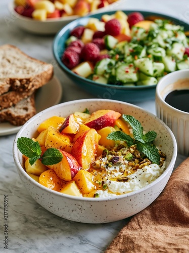 Bowl of fruit salad on a white marble countertop. the salad is made up of sliced peaches, raspberries, and cucumbers, and is garnished with fresh mint leaves.