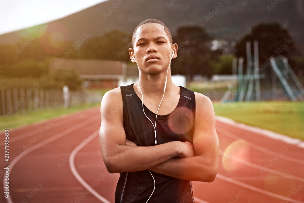 Obraz premium Fitness, portrait and teenager in stadium with earphones, music and crossed arms for sports event. Athlete, runner and African person with audio, track and serious for exercise, training and practice