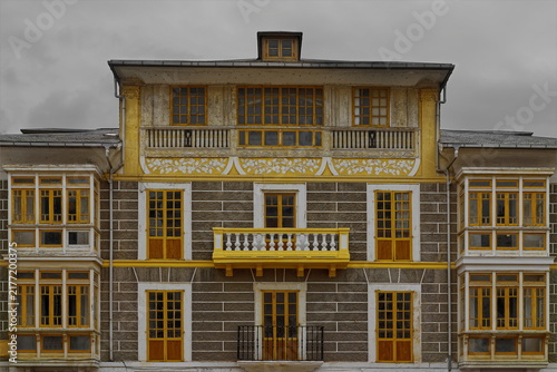 Facade of 'cube' style Indiano house of plastered walls painted gray with white bands, yellow decoration, and side oriels. Luarca-Asturias-Spain-022