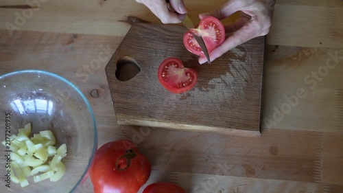 Woman's hands slicing fresh red tomatoes on wooden cutting board and putting them into glass bowl for vegetable salad