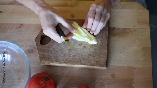 Woman's hands chopping sweet bell pepper on wooden cutting board for healthy salad meal preparation in kitchen