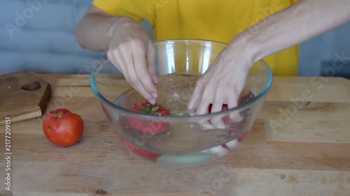 Person washing fresh ripe tomatoes in a glass bowl of water in a kitchen for healthy cooking