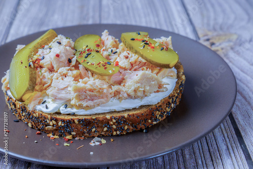 Obraz na płótnie Open faced sandwich presenting flaked tuna, creamy cheese, and sliced pickles on seeded bread