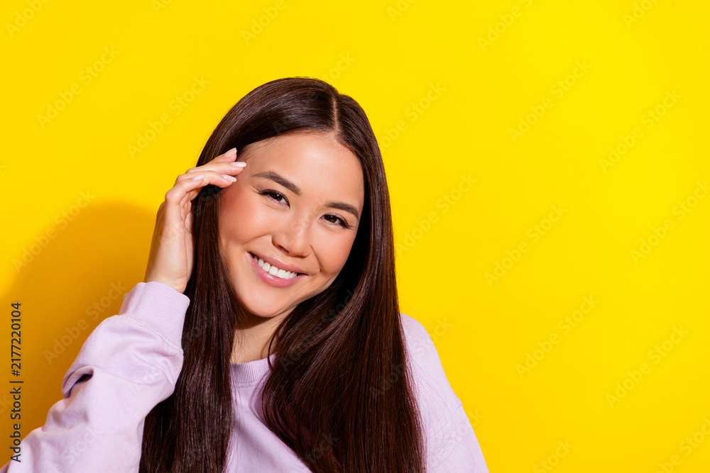 Fototapeta premium Smiling young woman with long dark hair posing against a bright yellow background, casual portrait conveying happiness, confidence and friendly warmth for lifestyle and beauty concepts