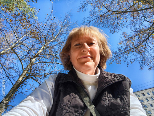Foto Mature woman enjoys a sunny moment outdoors while taking a selfie among the tree
