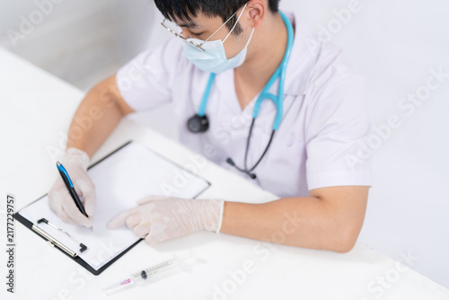 A male doctor wears a mask and works on online data reports to demonstrate vaccine preparation and clinical research in modern medical technologies for disease treatment.