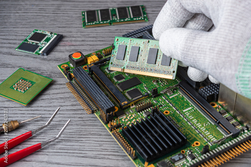 Technician works on a computer motherboard in a workshop while handling memory chips and tools