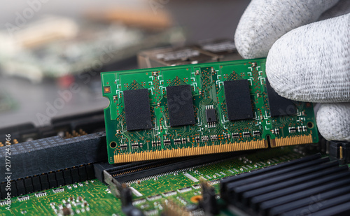 Person installs computer memory in a circuit board at a tech repair shop during daytime
