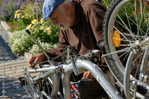 Cuadro en lienzo Old man repairs bicycle in a garden during the daytime, focused on the chain and