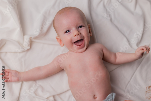 4‑month‑old baby in diapers is lying on the bed, viewed from above. Portrait of the baby against a light background.