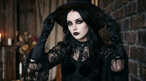 Young fashion model with gothic makeup and long black gloves posing in an elegant Halloween look, featuring dramatic eyes, pale skin, dark lips and a mysterious glamorous expression.