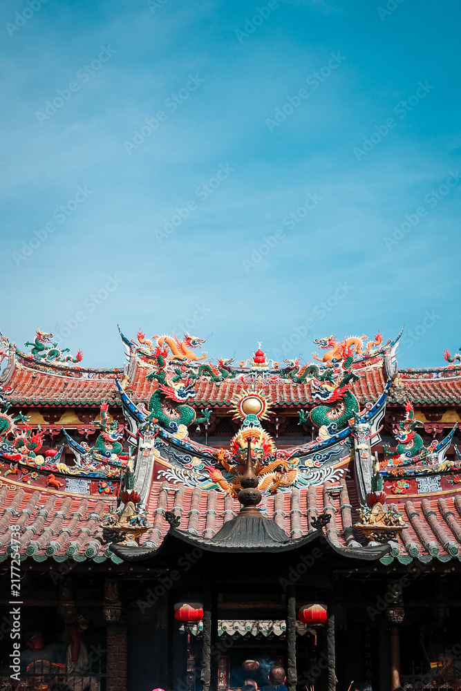 Fototapeta premium Porcelain sculptures of two dragons on the roof of a temple in Quanzhou contrast with the blue sky