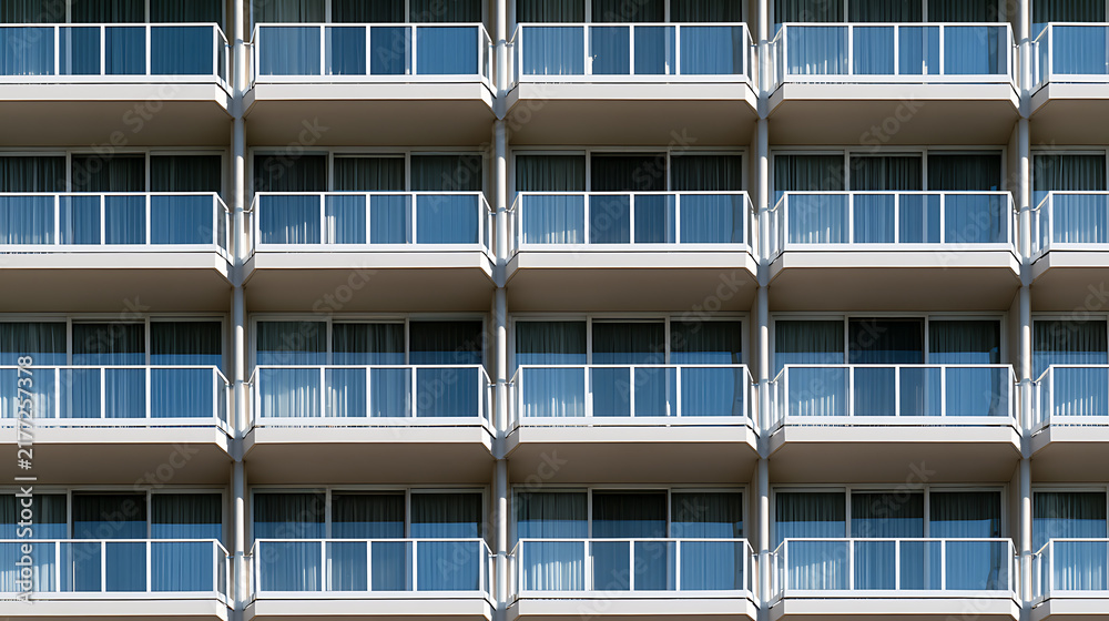 Obraz premium Modern hotel architecture facade detail with symmetrical rows of identical balconies and glass windows for commercial real estate concept
