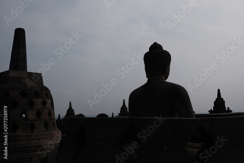 фотографія Silhouette of Seated Buddha Statue and Stupa Against Overcast Sky at Borobudur T