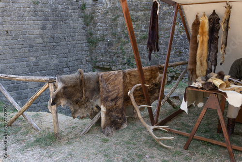 Medieval camp displaying animal pelts, fox furs, and deer antlers against an ancient stone wall background.