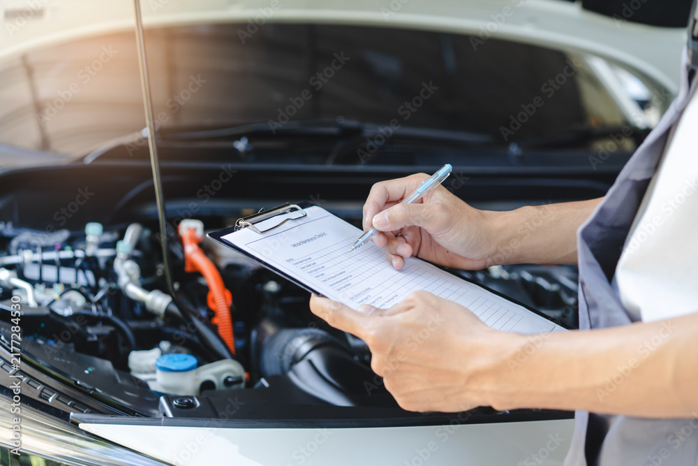 Obraz premium Auto check up and car service shop concept. Mechanic writing job checklist to clipboard to estimate repair quotation to client at workshop garage.