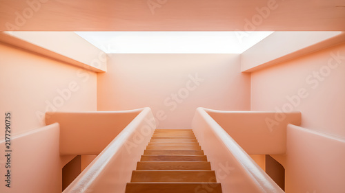 Wooden staircase ascending between peach colored walls with bright skylight above