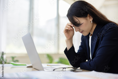 Young Japanese businesswoman with her hand on her forehead looking down at a desk