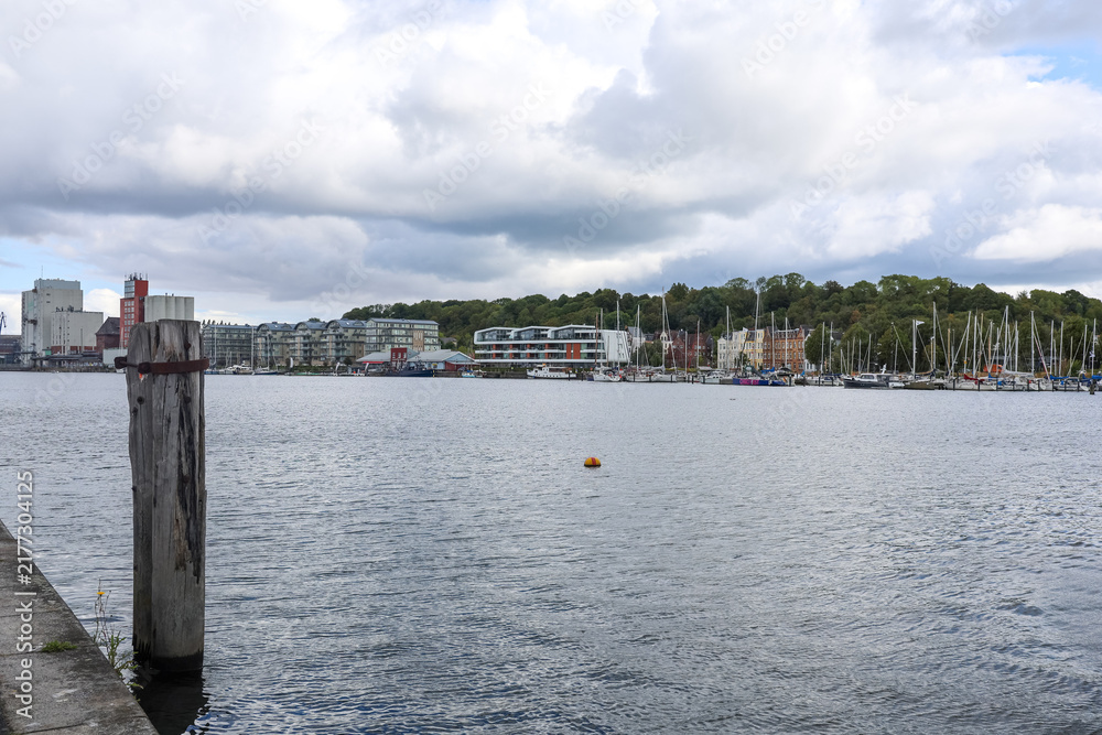 Obraz premium Flensburg, Germany - 17. August 2026: Waterfront view showing marina, city buildings, and industrial port