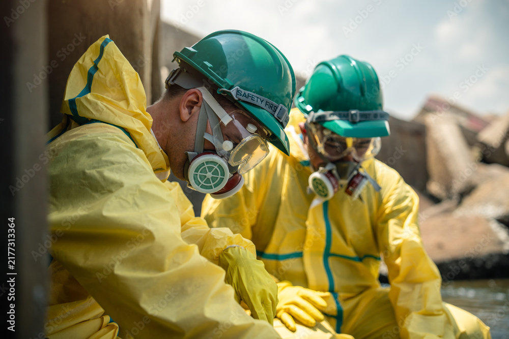 Fototapeta premium Hazmat Workers Conduct Environmental Safety Inspection Near Contaminated Industrial Drainage Infrastructure While Wearing Protective Suits, Respirators, Helmets, Goggles, and Gloves