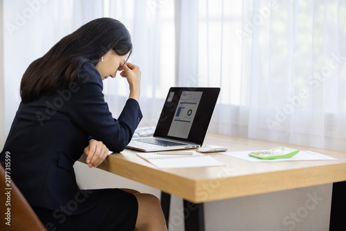 Rear view of a young Japanese businesswoman with her hand on her forehead looking down at a desk