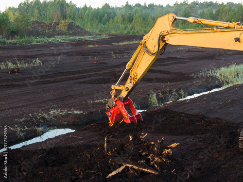 Konstfotografi Close up shot of yellow excavator arm with specialized red hydraulic bucket attachment digging into dark peat soil on industrial bog field in Estonia